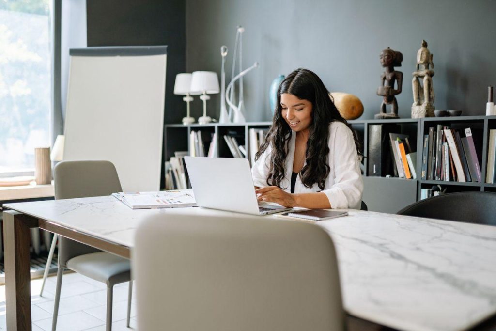 Entrepreneure souriante travaillant sur son ordinateur portable dans un bureau privé élégant avec bibliothèque